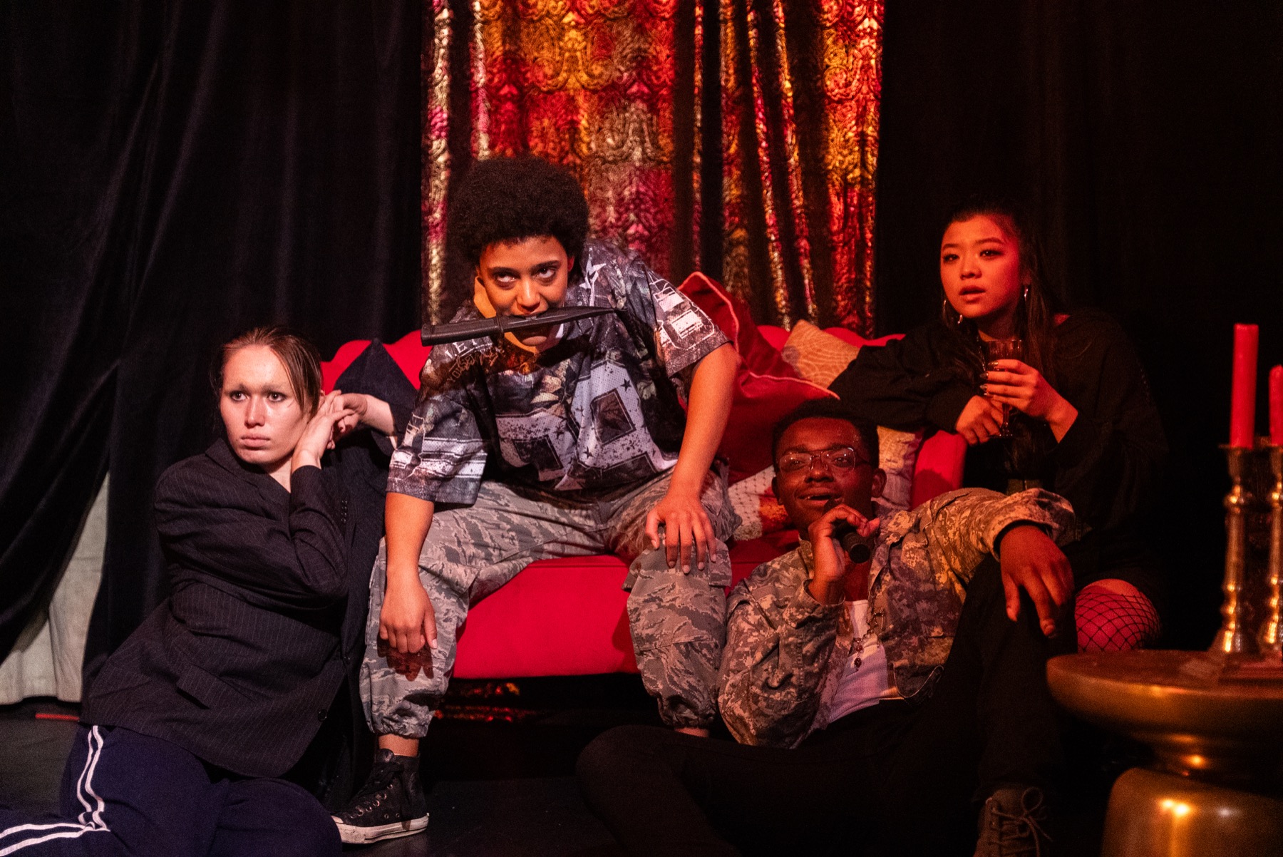 Four performers gather on the red couch in DECAPITATRIX