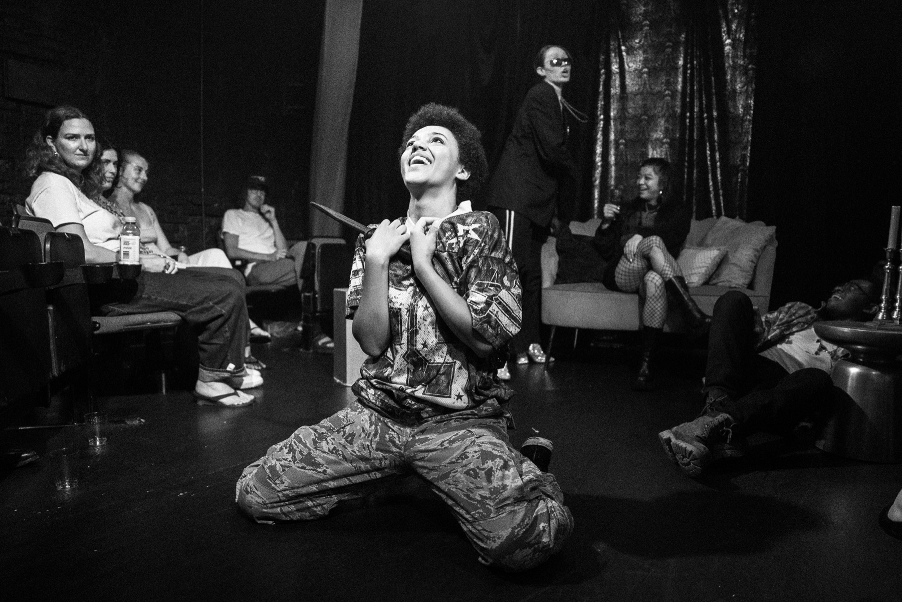 The Page kneels with a knife in a black-and-white DECAPITATRIX production photo