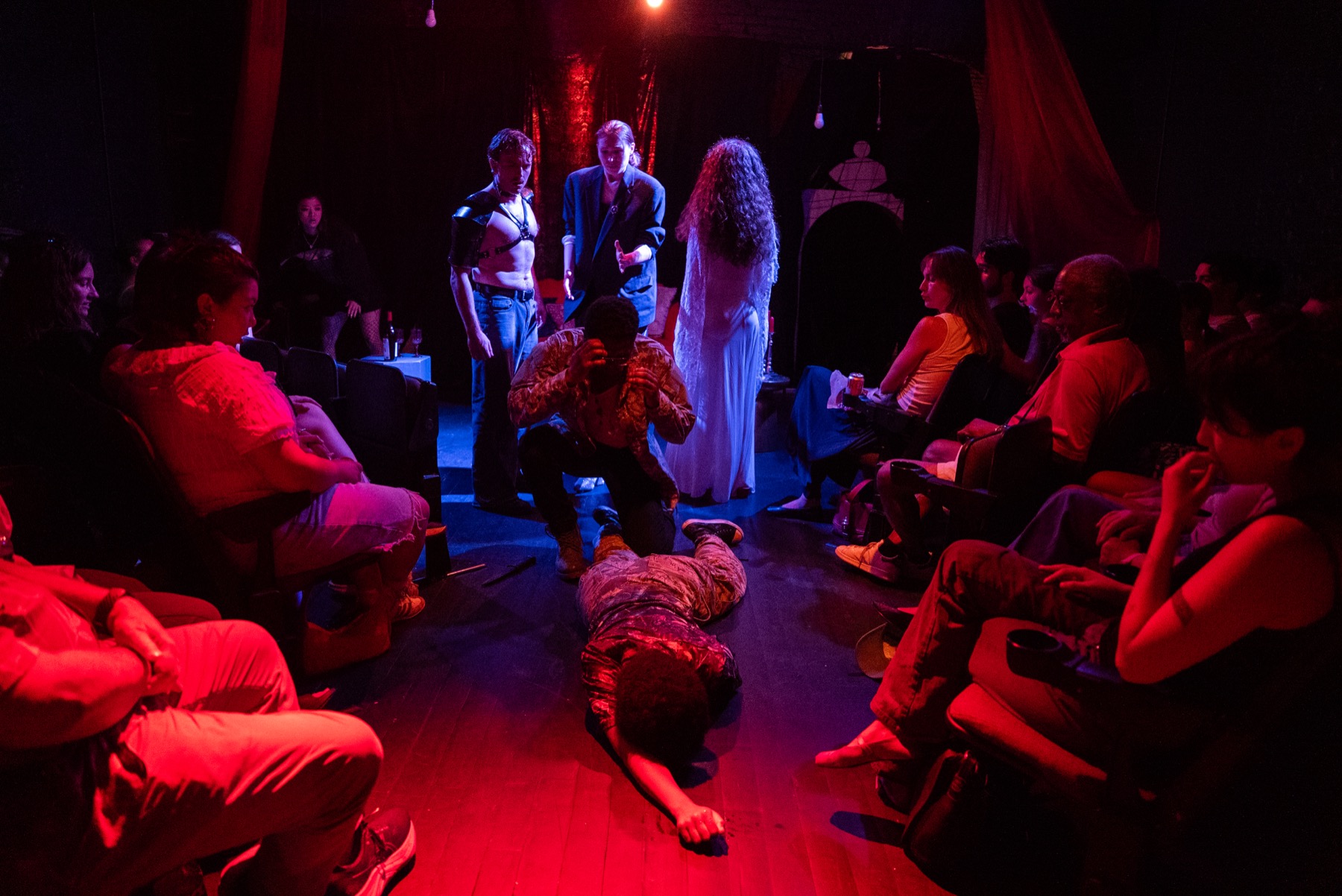 Audience surrounds the performers in a red-lit DECAPITATRIX production photo