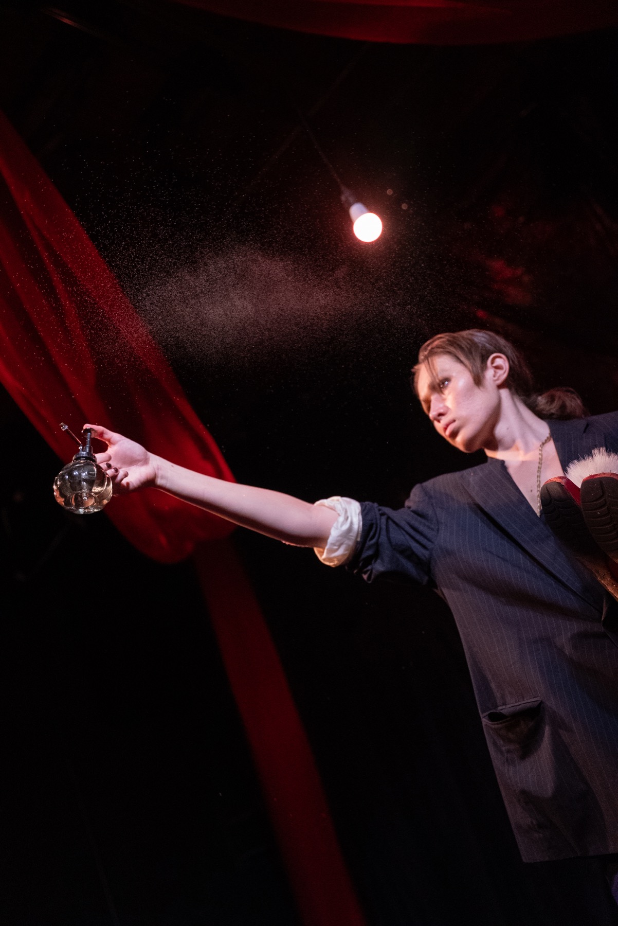 A performer sprays mist under red light during DECAPITATRIX