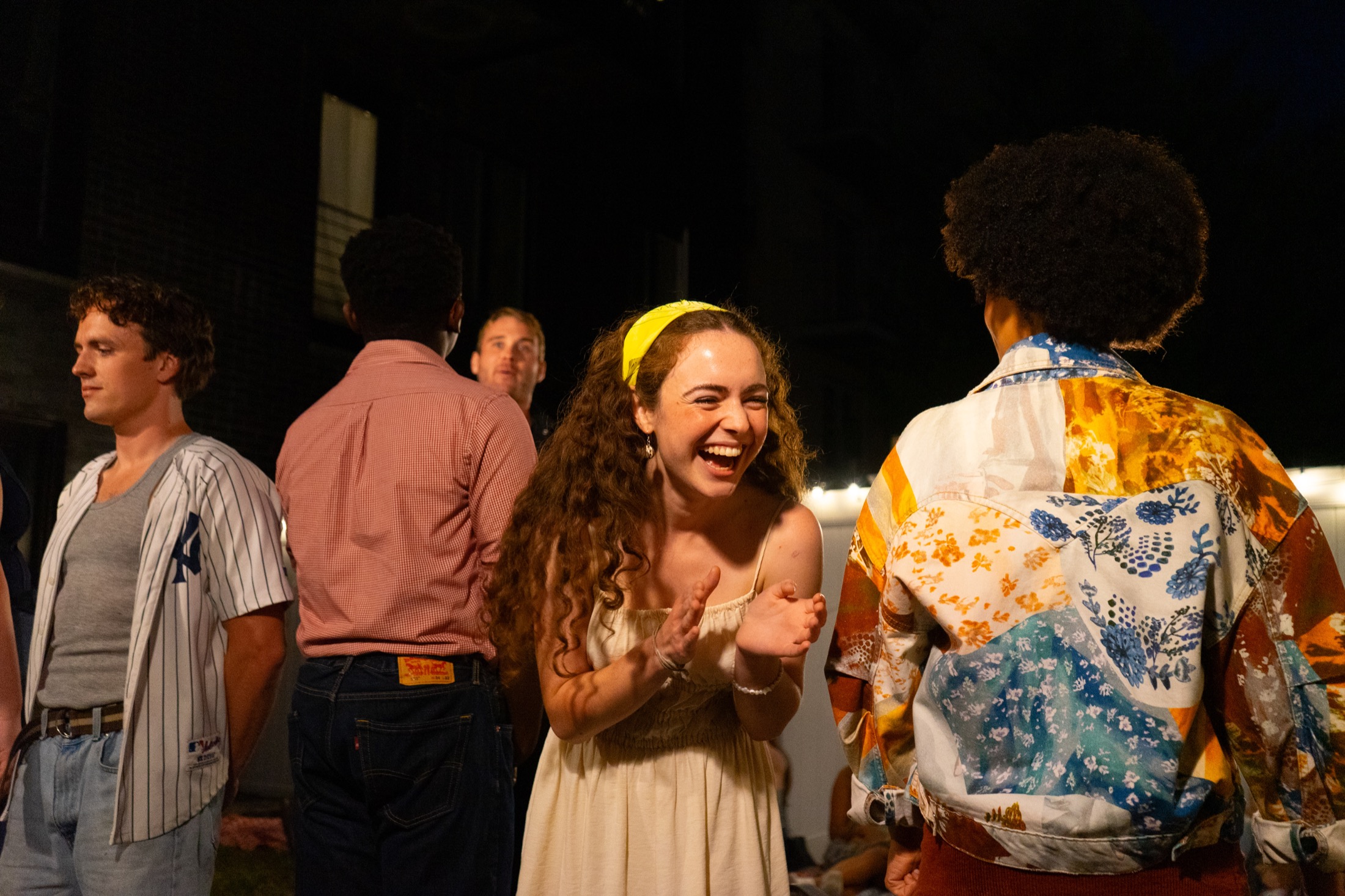 Emily laughs in a cream dress among performers during Our Town