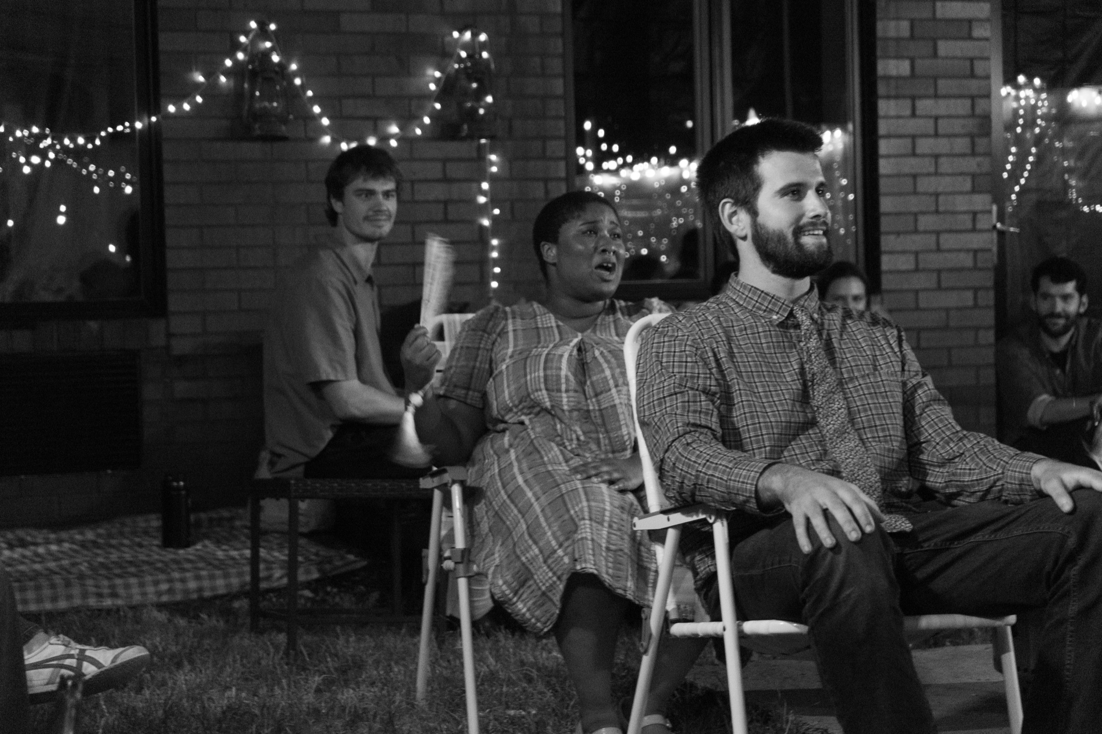 A group of performers sits near lawn chairs and a fire pit during Our Town