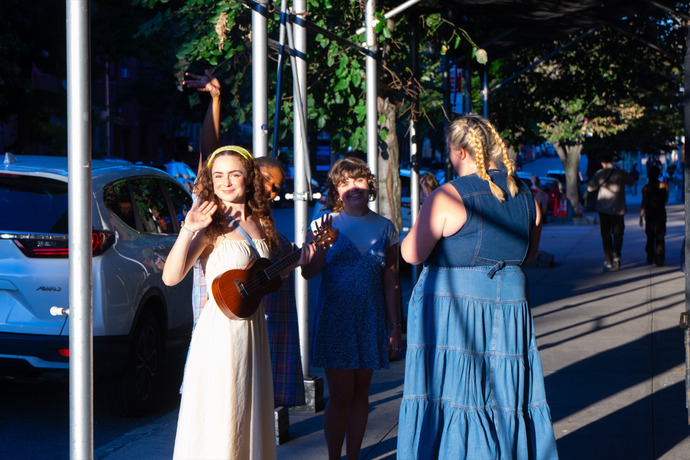 A performer with a ukulele waves on the sidewalk before Our Town