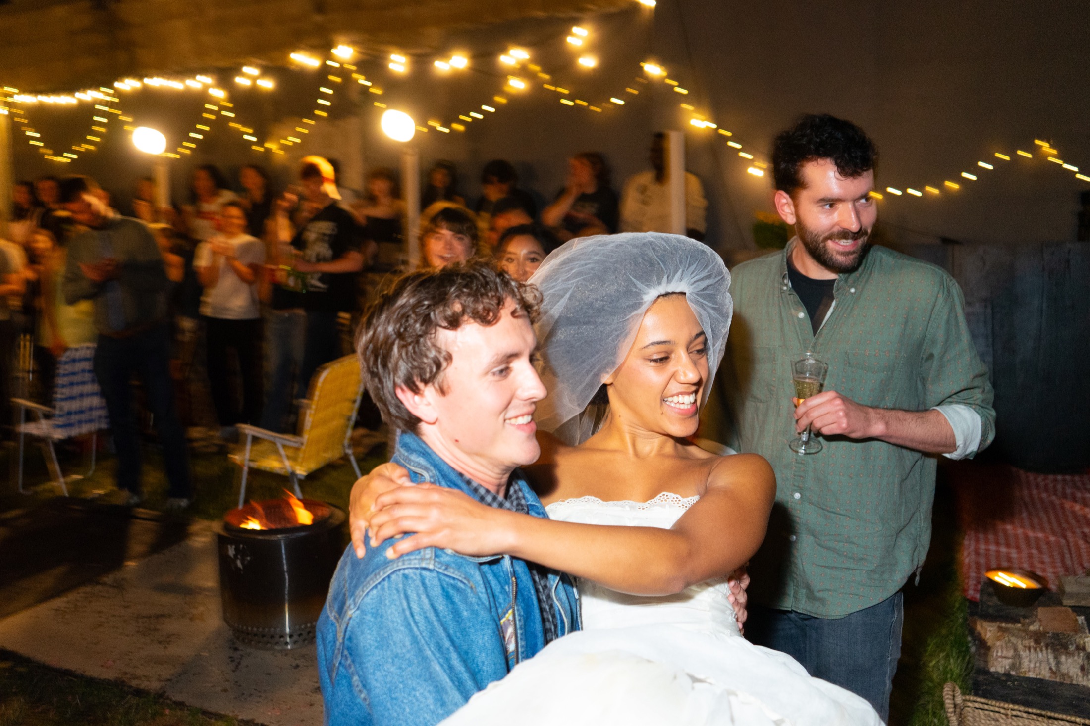 George and Emily celebrate among guests at night under string lights