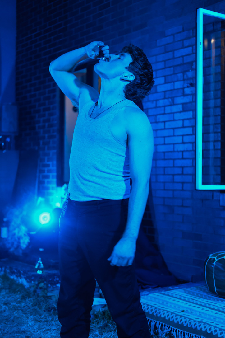 Romeo drinks from a small bottle in blue light