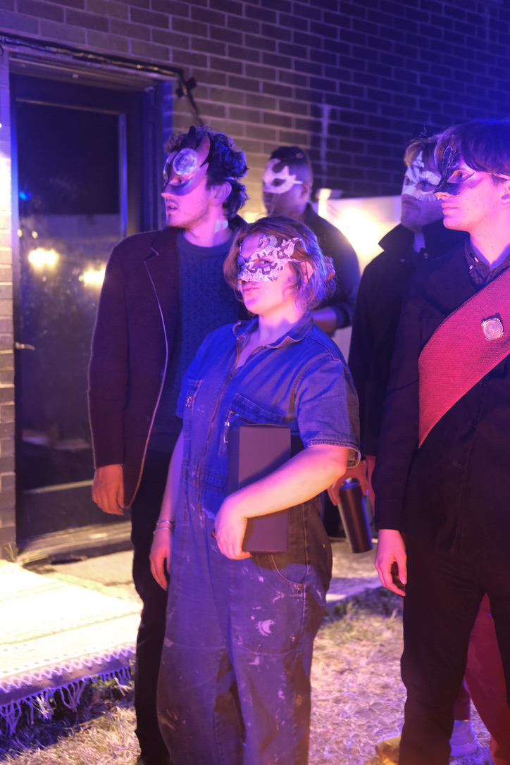 A masked group of performers stands in purple light