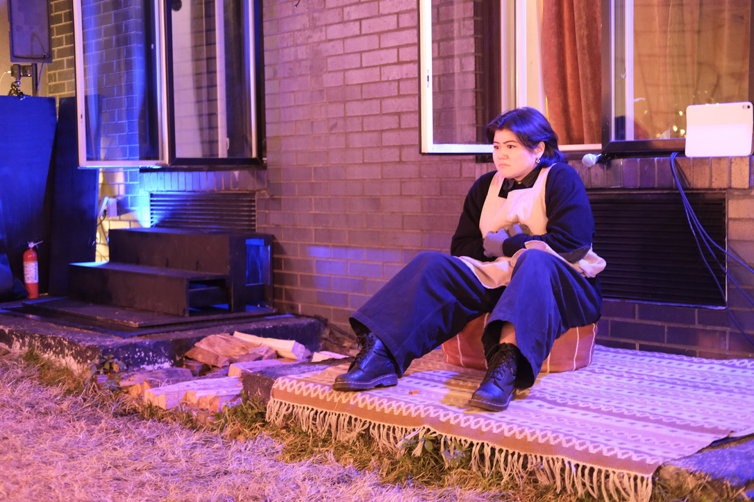The Nurse sits alone on a rug outside a brick building