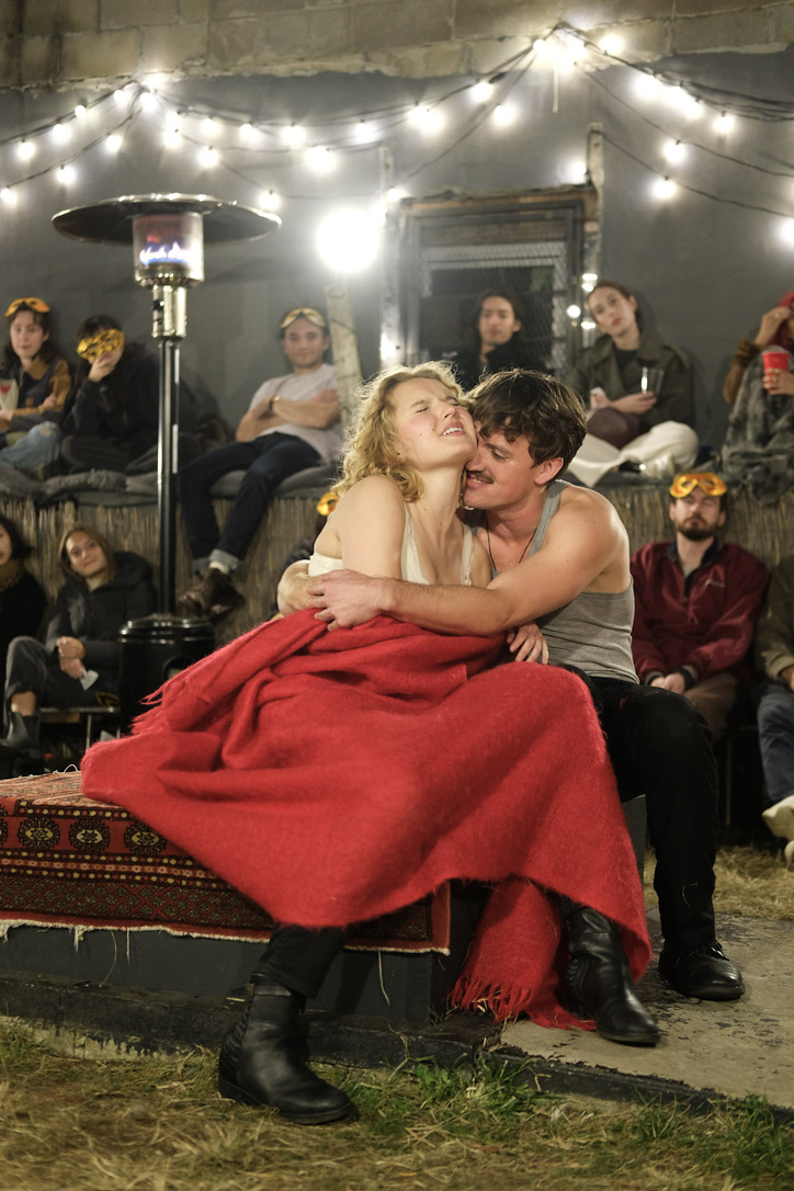 Romeo embraces Juliet on a red blanket while audience members watch