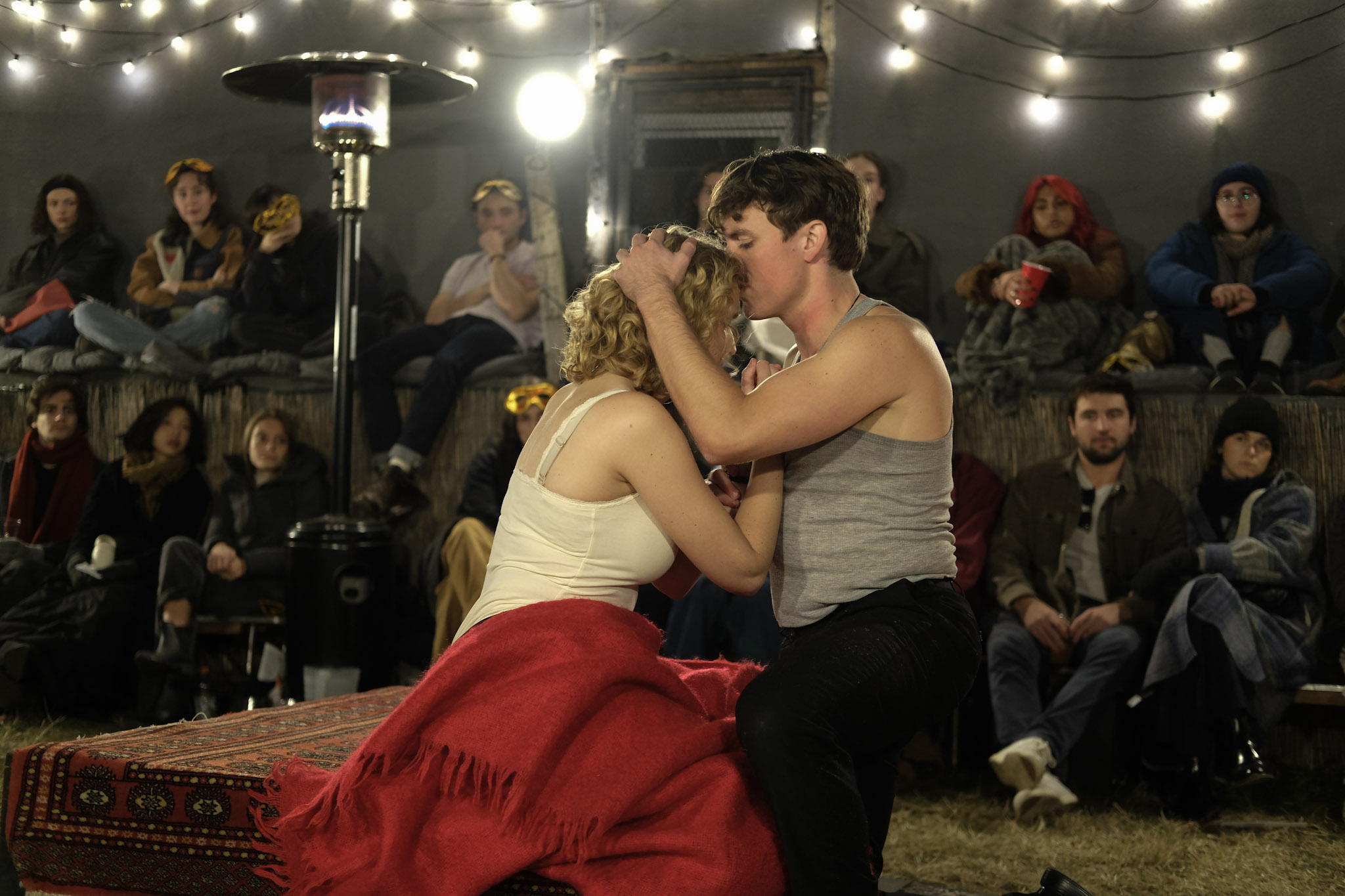 Romeo and Juliet seated together under string lights with audience members surrounding them