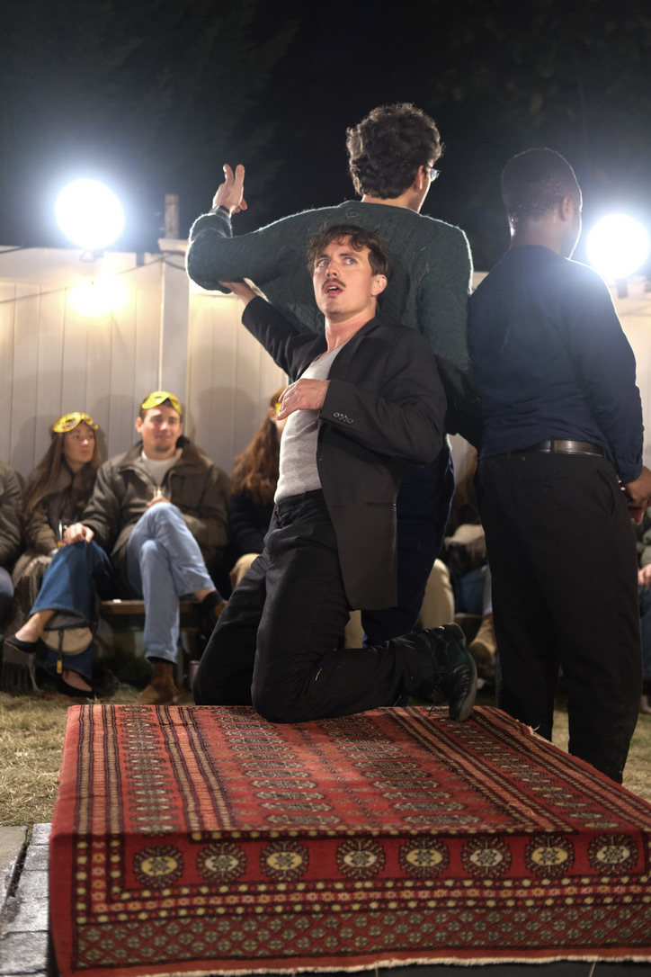 Romeo kneels on a rug before audience members