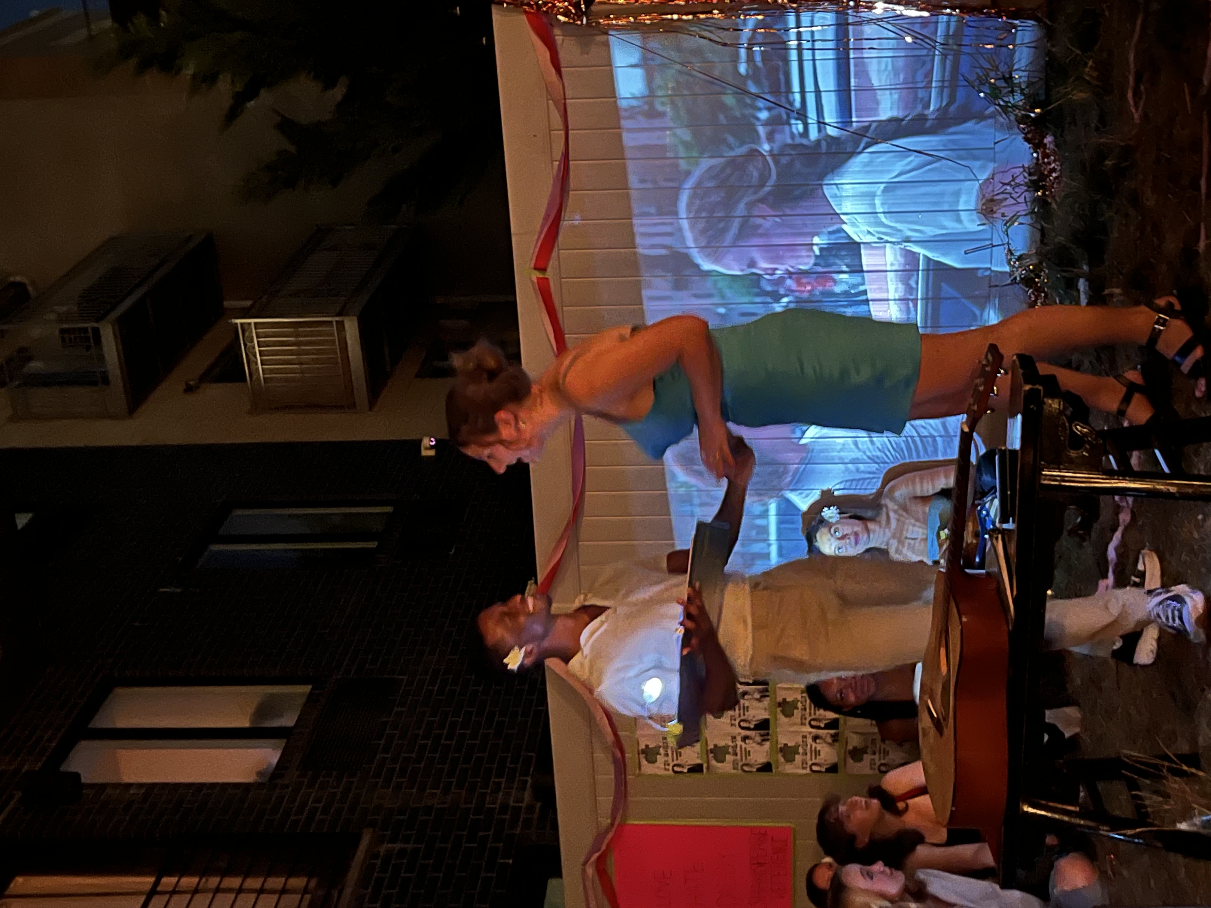 Two performers sing in front of a backyard projection