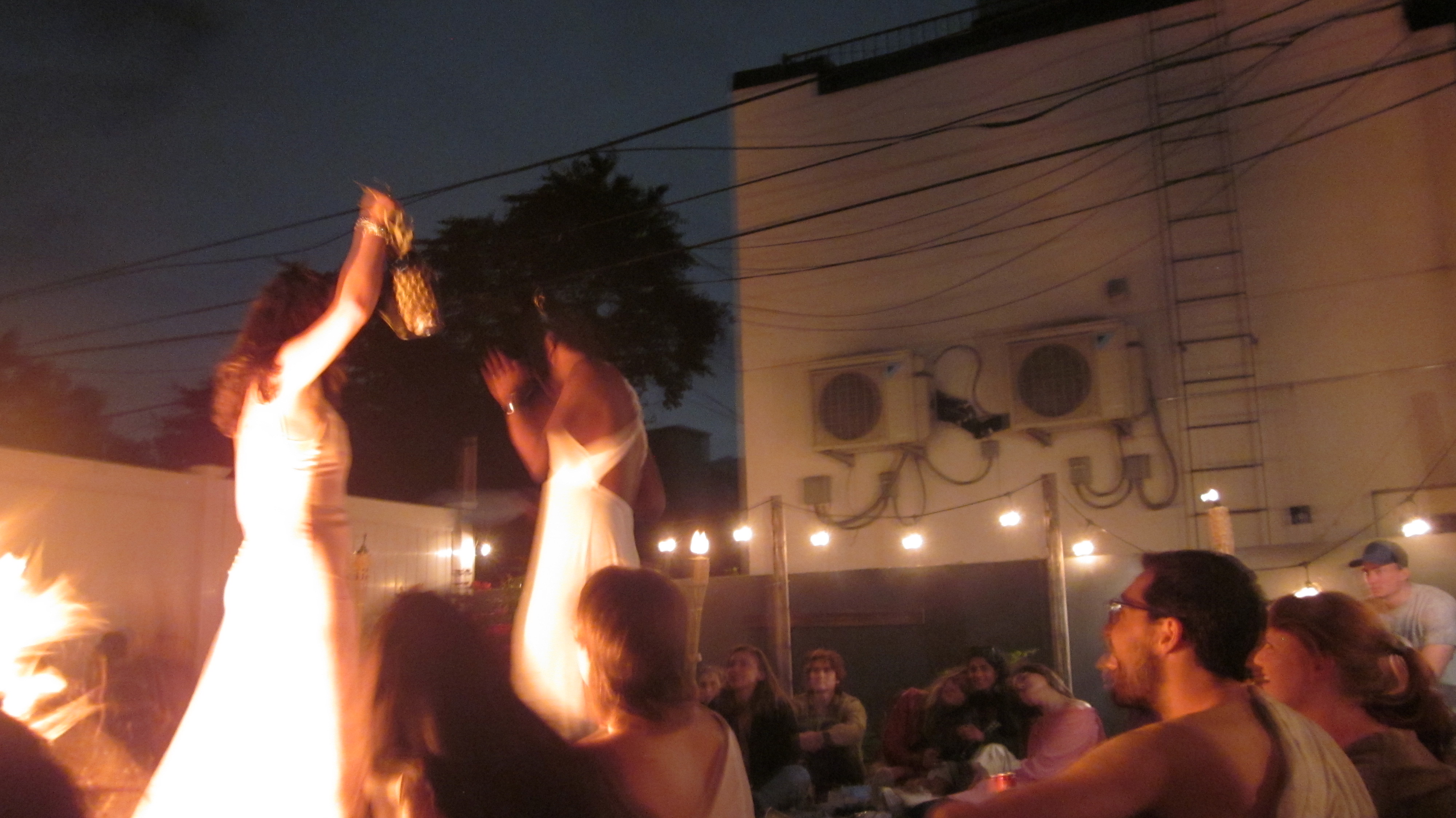 A firelit Bacchae ritual with performers and audience gathered in a backyard