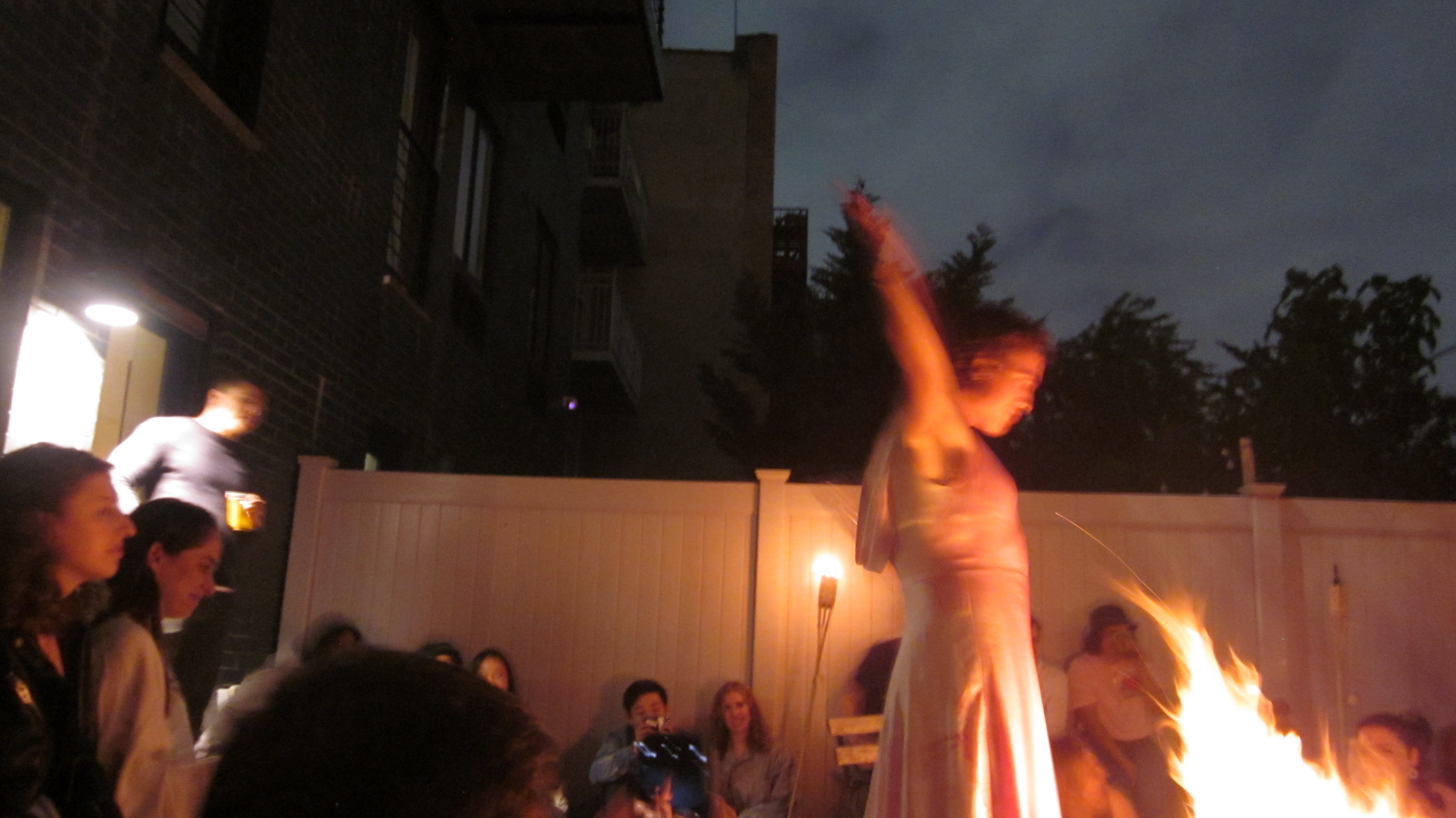 A performer moves beside a backyard fire in The Bacchae