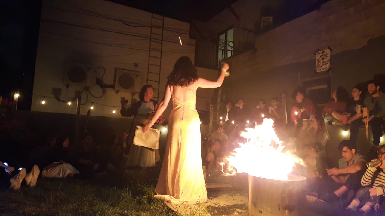 A firelit ritual scene from The Bacchae with performers and audience gathered in a backyard