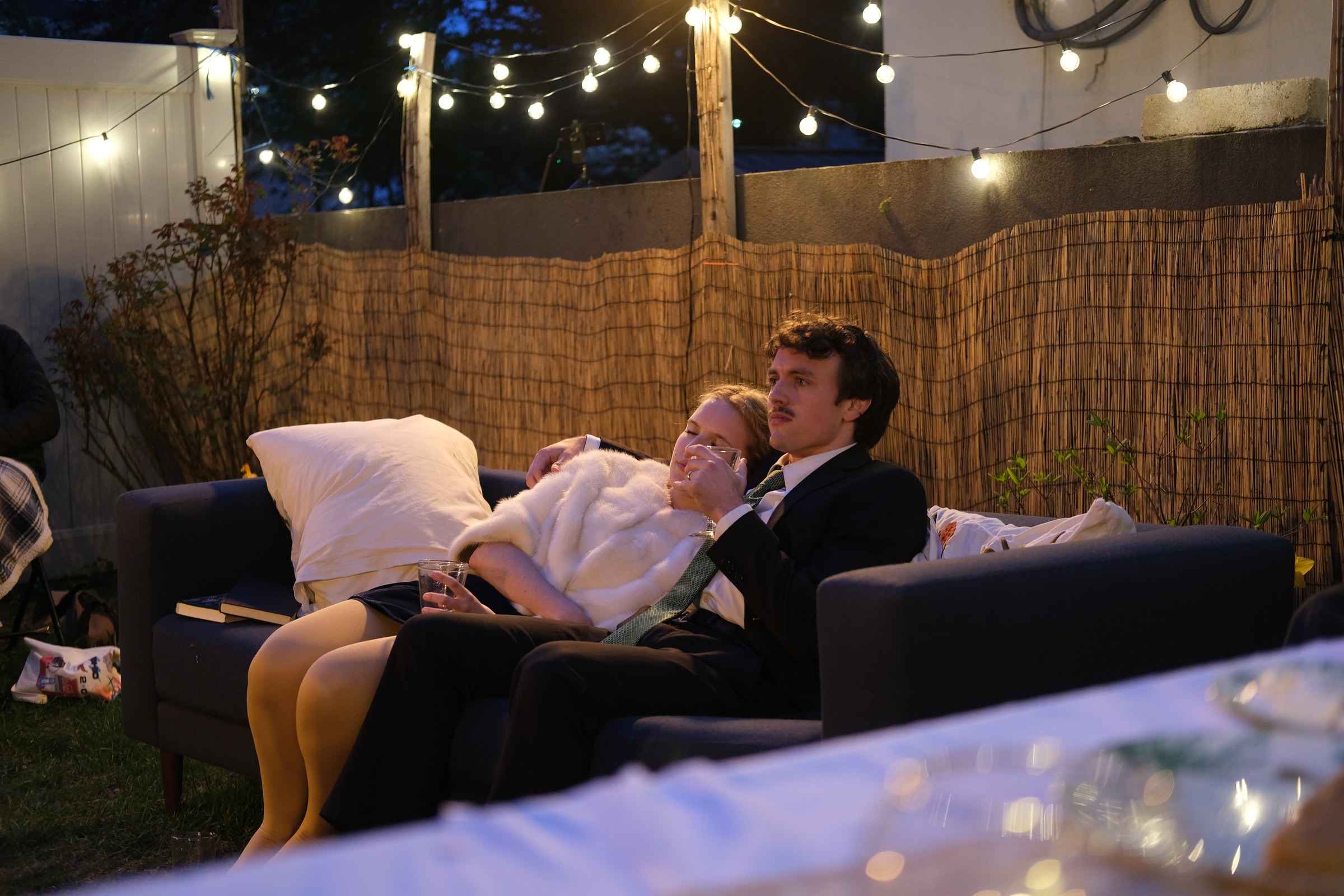 Honey and Nick lounge on an outdoor couch during the dinner party