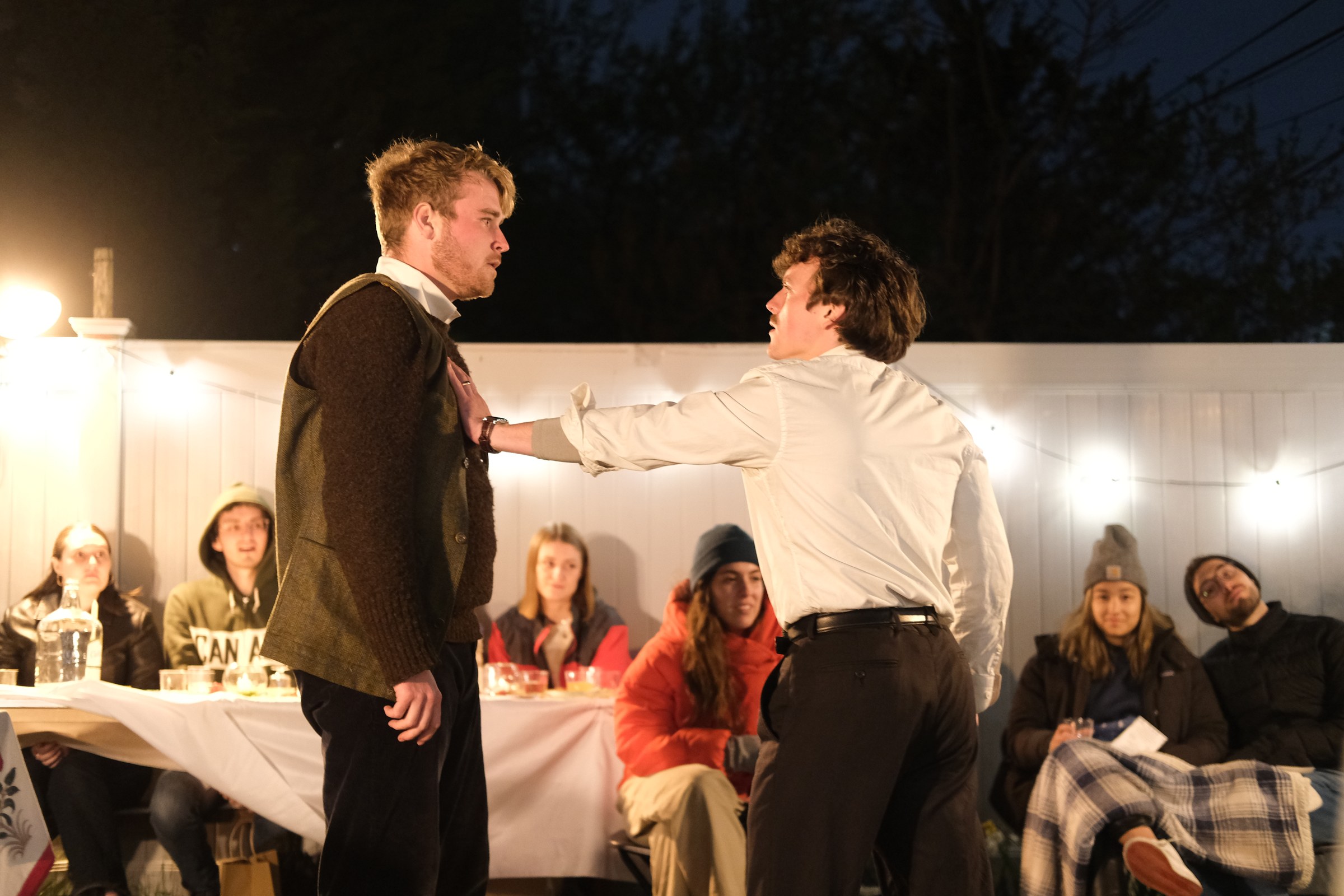 Nick grips George by the shirt in front of seated dinner guests